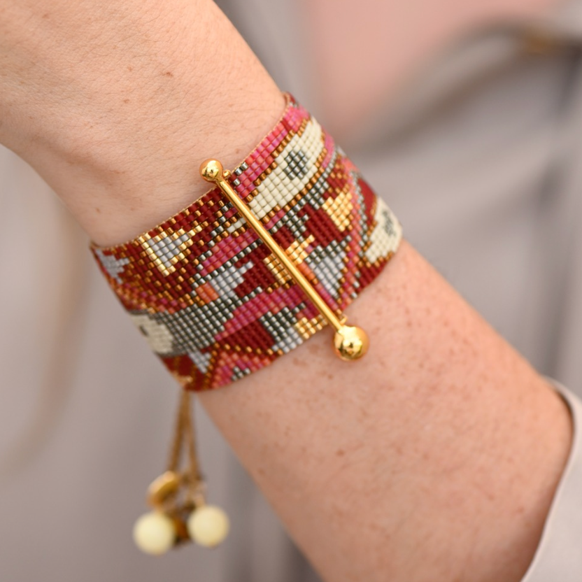 Close-up of a colorful beaded bracelet with gold accents on a wrist against a neutral background