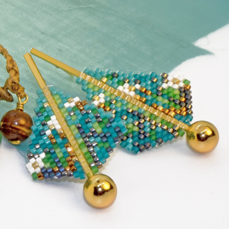 Beaded leaf-shaped brooch with gold and blue beads on a light green background