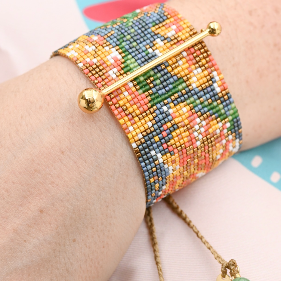 Colorful beaded bracelet with gold accents on a wrist against a colorful background